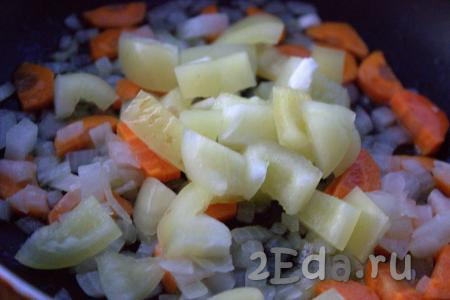 Болгарский перец, очищенный от перегородок и семян, нарезать средними кубиками и выложить в сковороду к луку и моркови, перемешать. Продолжать обжаривать овощи на среднем огне, периодически помешивая, в течение 5-7 минут.