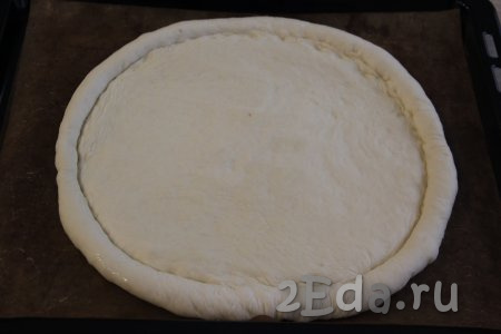 Тесто обмять и выложить на противень, застеленный пергаментом. Руки смазать маслом и сформировать из теста круглую пиццу диаметром, примерно, 28-29 см с высоким краешком. Оставить основу на минут 15-20.
