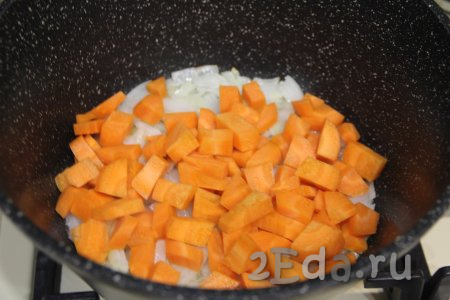 К луку, обжаренному до прозрачности, выложить морковку, нарезанную на средние кубики, перемешать и обжаривать овощи вместе 3-4 минуты, периодически помешивая.