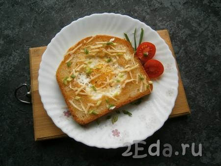 Яичницу, приготовленную в хлебе, переложить со сковороды на тарелку, посолить и поперчить, посыпать натертым сыром и измельченным зеленым лучком. 