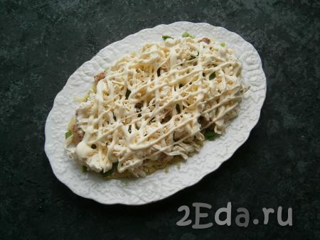 Следующим слоем выложить плавленный сыр, натертый на крупной терке, нанести сеточку из майонеза.
