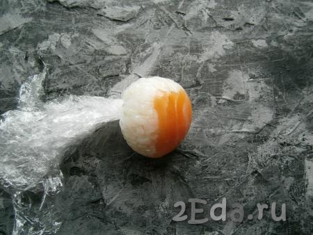 Аккуратно, чтобы рисовый шарик не сдвинулся, собрать края пленки кверху и закрутить их. Закручивать нужно плотно и крепко, чтобы шарик риса приобрел правильную круглую форму.