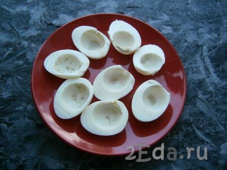 Разрезать каждое яйцо пополам вдоль, вынуть желтки. Белки разместить на тарелке, на которой будем подавать блюдо.