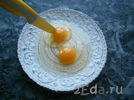 В тёплую тарелку разбить аккуратно 2 яйца. Обязательно острием ножа проткнуть желтки - это нужно сделать для того, чтобы они вдруг не разбрызгались внутри печи.