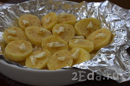 Затем картофель посолить, приправить специями по вкусу. Положить на каждую половинку картошины по небольшому кусочку сливочного масла.