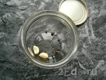 На дно простерилизованной сухой банки поместить 2 зубчика чеснока, горошины чёрного перца, гвоздику, горошины душистого перца.
