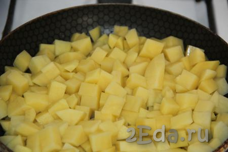 Влить в сковороду растительное масло, затем выложить картошку, нарезанную на кубики, и жарить на сильном огне минут 5, периодически перемешивая картофель.