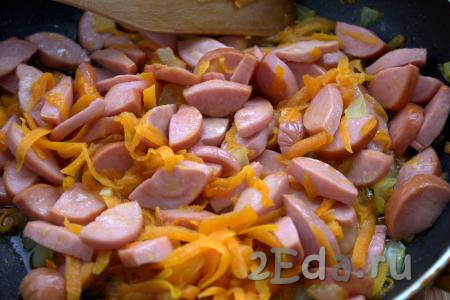 Добавить нарезанные сосиски в сковороду и, помешивая, обжаривать 2-3 минуты вместе с луком и морковкой.
