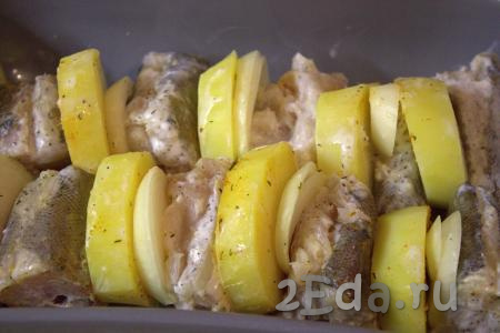 В жаропрочную форму, чередуя, выложить кружочки картофеля и лука, порционные кусочки хека (как на фото).