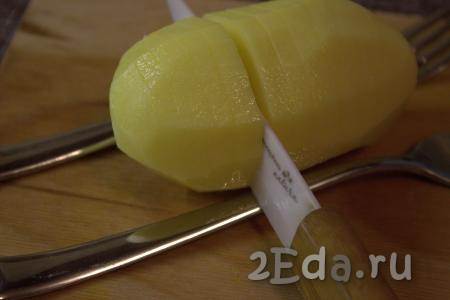 Острым ножом на поверхности каждой картофелины сделать поперечные надрезы на расстоянии, примерно, 0,5 сантиметра, не дорезая до конца. Удобно делать надрезы, положив картофелину между двух вилок или ложек (как на фото). Вилки (или ложки) станут "ограничителем", который поможет аккуратно надрезать клубень картофеля, не разрезав его полностью.