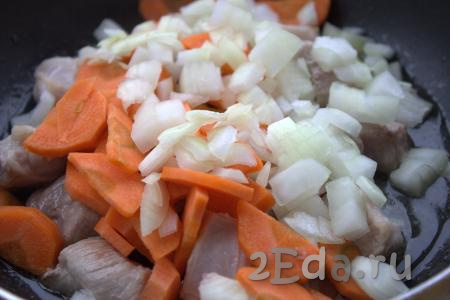 Уменьшить огонь до среднего, к обжаренным кусочкам свинины добавить нарезанные морковь и лук, слегка посолить и перемешать. Готовить овощи с мясом на среднем огне 7-10 минут, не забывая периодически помешивать.
