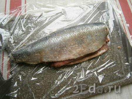 Селёдку поместить на пищевую плёнку и хорошенько натереть рыбку внутри и снаружи солью, смешанной со специями.