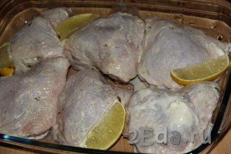 Замаринованные кусочки курицы выложить в жаропрочную форму.  Оставшийся маринад не нужно выливать в форму. Не использованную половинку лимона нарезать на дольки и выложить в форму поверх курицы.