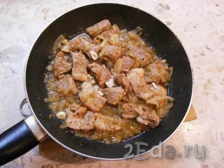 Обжарить свинину с луком в течение 4-5 минут, перемешивая. Затем влить горячую воду, добавить специи для мяса, соль по вкусу, прикрыть сковороду крышкой и тушить мясо на слабом огне 15-20 минут. Практически вся жидкость должна испариться. Добавить к мясу измельченный очищенный чеснок.
