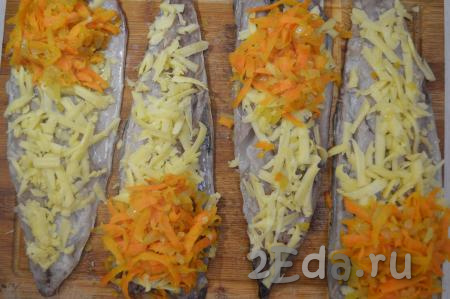 Филе скумбрии выложить кожей вниз. Каждое рыбное филе по всей длине равномерно посыпать натёртым сыром, затем на широкий край рыбки выложить по столовой ложке с горкой остывшей смеси морковки и лука.