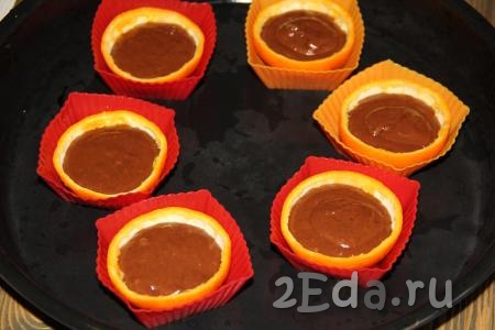 Наполнить апельсиновые чашечки тестом, заполняя их на 1/3 объёма. Выпекать шоколадные капкейки в разогретой духовке при температуре 180 градусов, примерно, 25-30 минут. Готовность проверить сухой зубочисткой (зубочистка должна остаться сухой при прокалывании готовой выпечки). Готовые капкейки остудить.