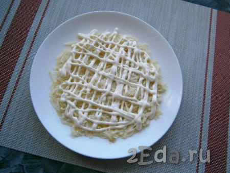 На плоскую тарелку выложить слой натёртого на средней терке картофеля, посолить и нанести сеточку из майонеза.