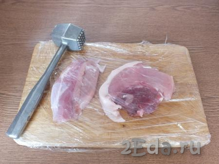 Разделочную доску оберните пищевой плёнкой. На доску положите нарезанную свинину, сверху прикройте плёнкой и отбейте мясо молоточком.