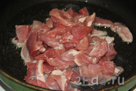 В сковороду влить немного растительного масла, разогреть. Выложить в разогретое масло кусочки свинины.