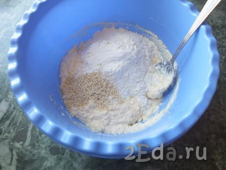 Добавьте к творожно-масляной массе разрыхлитель для теста, 2 чайные ложки кунжута, часть муки, перемешайте ложкой.