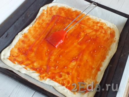 Противень застелите бумагой для выпечки. Выложите раскатанное слоёное тесто. Сделайте частые проколы вилкой. Смажьте тесто томатным соусом, не доходя до краёв по 1 см.