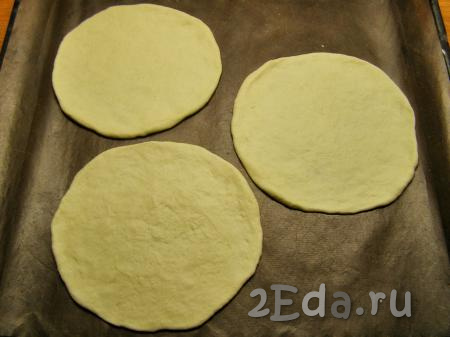 К этому времени тесто уже должно будет подойти и увеличиться в объёме, примерно, в два раза. Разминаем его и делим на 8-9 одинаковых кусочков. Присыпаем доску мукой и раскатываем каждый кусочек теста в тонкую круглую лепёшку диаметром 12-14 см. Перекладываем несколько лепёшек на противень, застеленный ковриком для выпечки (или пекарской бумагой).
