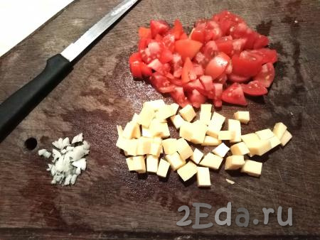 Пока запекаются половинки баклажана, нарезаем кубиками сыр и помидор. Очищаем зубчик чеснока и мелко нарезаем.