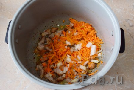 Лук и морковь очистите от кожуры и ополосните в проточной воде. Затем лук мелко нарежьте, а морковь натрите на тёрке. Когда свинина обжарится в течение 8-10 минут, добавьте к ней морковку с луком, перемешайте и обжаривайте минут 5-7, не забывая иногда помешивать.