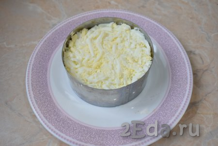 Отварные яйца очистите от скорлупы и натрите на крупной тёрке. Выложите их в салатник. Немного прижмите, чтобы слой стал более плотным. Смажьте яйца небольшим слоем майонеза.