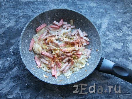 Обжарить лук с колбасой на сковороде, помешивая, в течение 3-4 минут, добавить специи и чёрный молотый перец, перемешать.