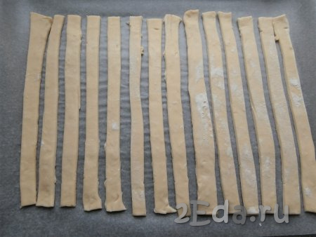 Пласты слоёного теста чуть разморозить и немного раскатать скалкой. Нарезать тесто на 14 узких длинных полос (у меня длина полос - 20-22 см, ширина - 1,5 см), выложить их на противень, застеленный пергаментом.