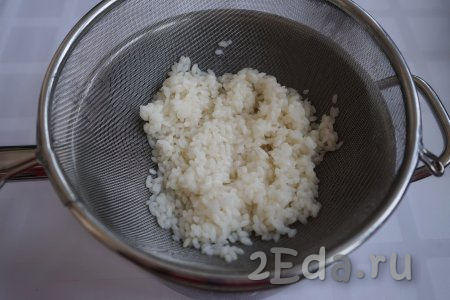 К этому времени рис уже дошёл до состояния полуготовности. Откидываем его на дуршлаг и промываем под холодной проточной водой, даём стечь лишней жидкости.