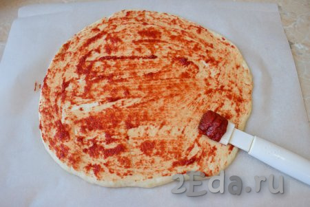 Подошедшее тесто разрежьте на 2 части (будем готовить 2 пиццы). Каждую часть теста на присыпанной мукой поверхности раскатайте в круг диаметром, примерно, 30 см. Выложите заготовки пиццы на бумагу для выпечки. Поверхность теста смажьте томатной пастой.