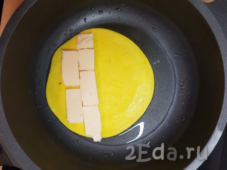 Когда желток прожарится (его верх перестанет быть жидким), чуть ближе к одному краю выложить ряд нарезанного пластинами сыра.