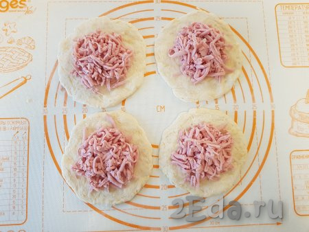 Натёртую колбасу (или сосиски) разделить на 4 равные части и выложить в центр каждого кружочка.