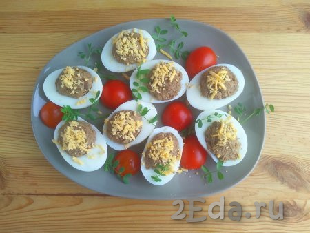 Яичные белки заполнить грибной массой, присыпать натёртым желтком. Выложить фаршированные яйца на тарелку для подачи. Блюдо, по желанию, можно украсить помидорами черри, свежей зеленью. Подать закуску к столу.