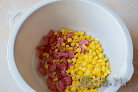 В достаточно большую миску выложите нарезанную колбасу, сюда же добавьте консервированную кукурузу (старайтесь выкладывать кукурузу без жидкости, в которой она находилась в банке).