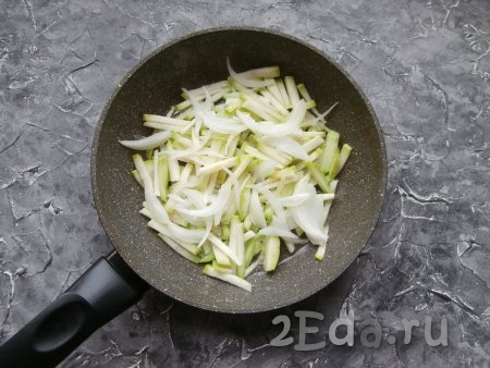 В сковороду влить растительное масло, разогреть, выложить кабачок, а также очищенный и нарезанный тонкими перьями репчатый лук.