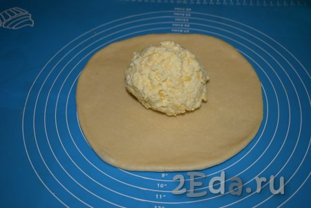 Достаём из морозилки один кусок теста и раскатываем в лепёшку диаметром, примерно, 22 см. Половину сырной начинки комкуем руками в шар и выкладываем в центр лепёшки.