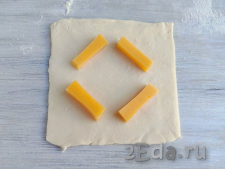 Сыр нарезать небольшими брусочками толщиной 0,7 см и длиной около 5 см. Выложить 4 кусочка сыра на каждую заготовку слойки (как на фото).