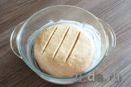 Возьмите форму для выпечки, смажьте её сливочным маслом. Из теста сформируйте шар и выложите его в форму. На поверхности шара сделайте 3 разреза острым ножом, прикройте полотенцем и оставьте в тепле на 30 минут.