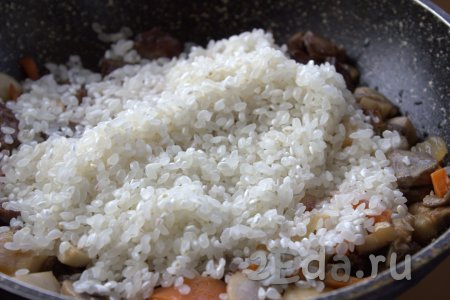 Рис хорошо промыть под проточной водой, добавить в сковороду к куриным сердечкам и овощам, разровнять.