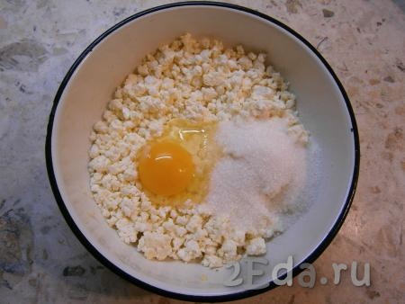 В творог добавить щепотку соли, сырое яйцо и всыпать сахар.