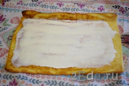 Когда бисквит остынет, разворачиваем его, убираем полотенце. Кладём развёрнутый бисквит на пищевую пленку, смазываем сметанным кремом.