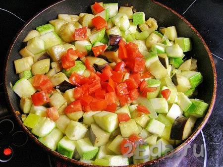 Вымытый помидор нарезаем на кубики среднего размера, добавляем его к обжаренным овощам и снова перемешиваем. Уменьшаем огонь до минимального, накрываем сковороду крышкой и тушим овощное рагу 20-25 минут.