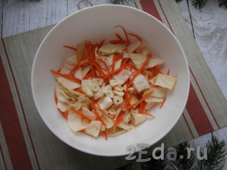 Посолить капусту с морковкой, немного помять руками, затем добавить зубчики чеснока, нарезанные на пластины.