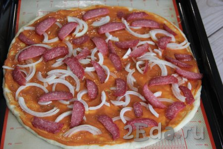 Выложить лук и колбасу на смазанную творожную основу пиццы. 