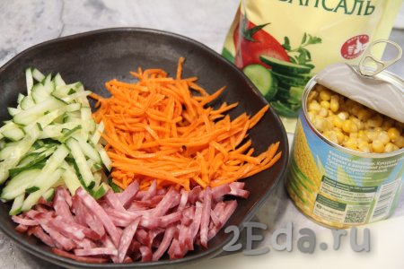 В салатнике соединить корейскую морковку, колбасу и огурец. Если полоски моркови очень длинные, тогда разрежьте их на несколько частей.