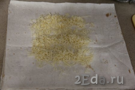 Взять одну отрезанную часть лаваша, на середину выложить часть сыра, натёртого на мелкой тёрке.
