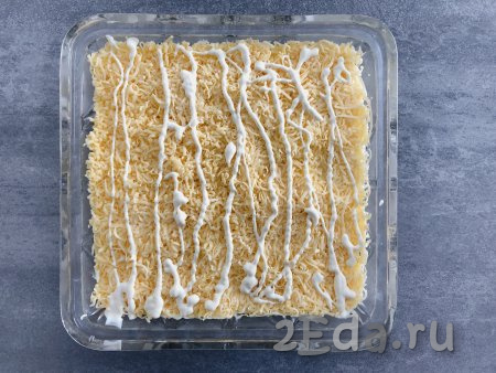 Следующим слоем равномерно раскладываем сыр, натёртый на мелкой тёрке, сверху наносим сеточку из майонеза.